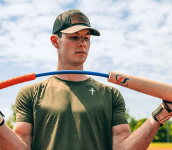 A man in a green T-shirt and baseball hat bends the Perfect Swings USA lag bat outside on a sunny day.