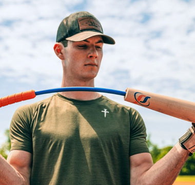 A man in a green T-shirt and baseball hat bends the Perfect Swings USA lag bat outside on a sunny day.