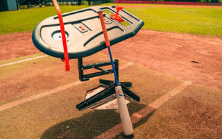 A close-up of the Perfect Swings USA Lag Bat propped up against the Swing Path Trainer IV on a baseball home plate.