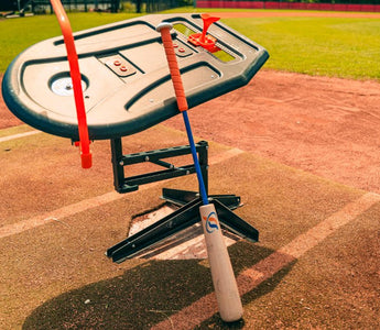 A close-up of the Perfect Swings USA Lag Bat propped up against the Swing Path Trainer IV on a baseball home plate.