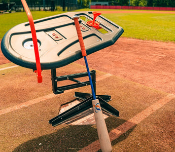 A close-up of the Perfect Swings USA Lag Bat leaning against the Swing Path Trainer over home plate of a baseball field.